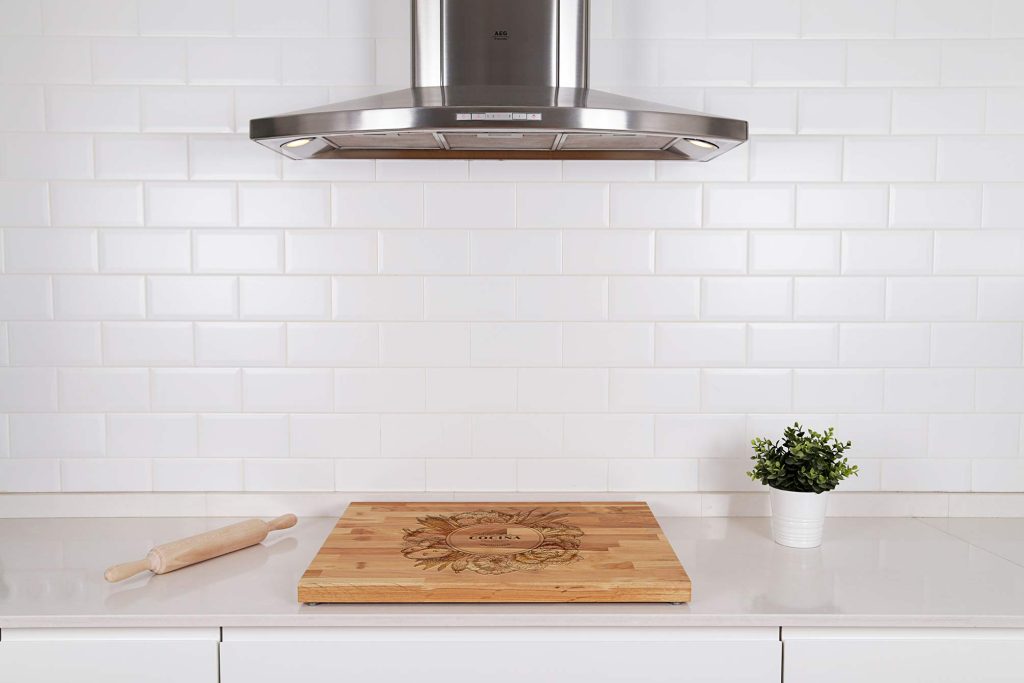 Plano detalle de la zona para cocinar en una cocina. Cubre vitrocerámica de madera, protegiendo la vitrocerámica, elementos decorativos alrededor.Campaña extractora en la parte superior.